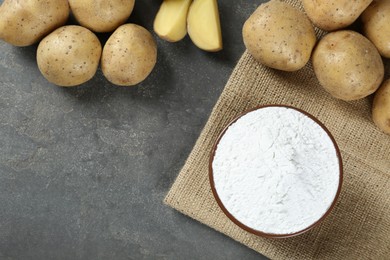 Bowl with starch and fresh potatoes on grey table, flat lay