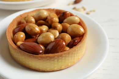 Photo of Tartlet with caramelized nuts on table, closeup. Tasty dessert