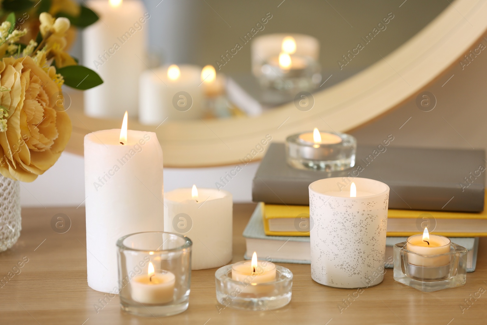 Photo of Beautiful burning candles, books and flowers on table at home