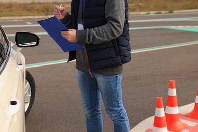 Instructor with clipboard near car outdoors, closeup. Driving school exam