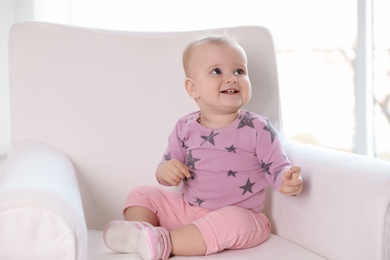 Cute baby girl sitting in armchair at home