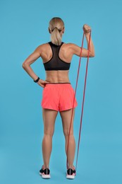 Photo of Woman exercising with elastic resistance band on light blue background, back view