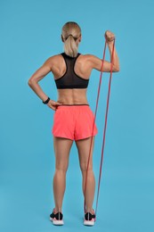 Woman exercising with elastic resistance band on light blue background, back view