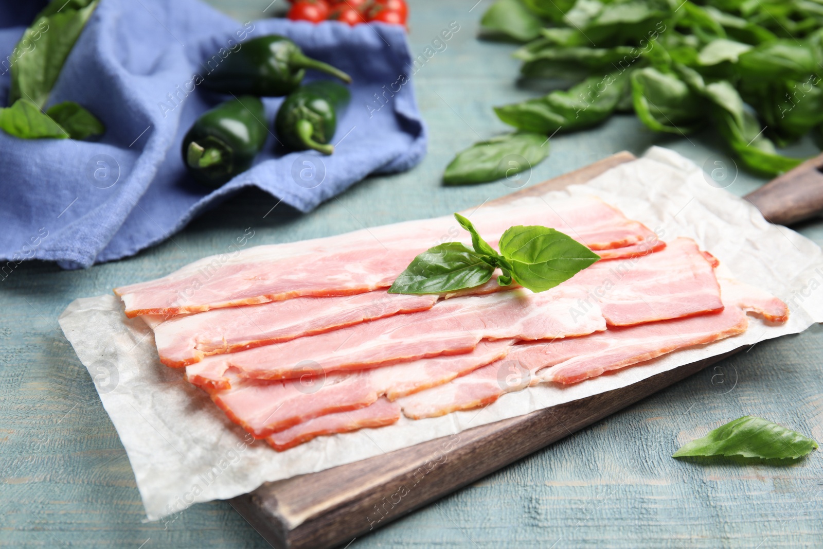 Photo of Board with sliced raw bacon on light blue wooden table