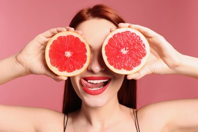 Photo of Beautiful redhead woman covering eyes with grapefruits on pink background