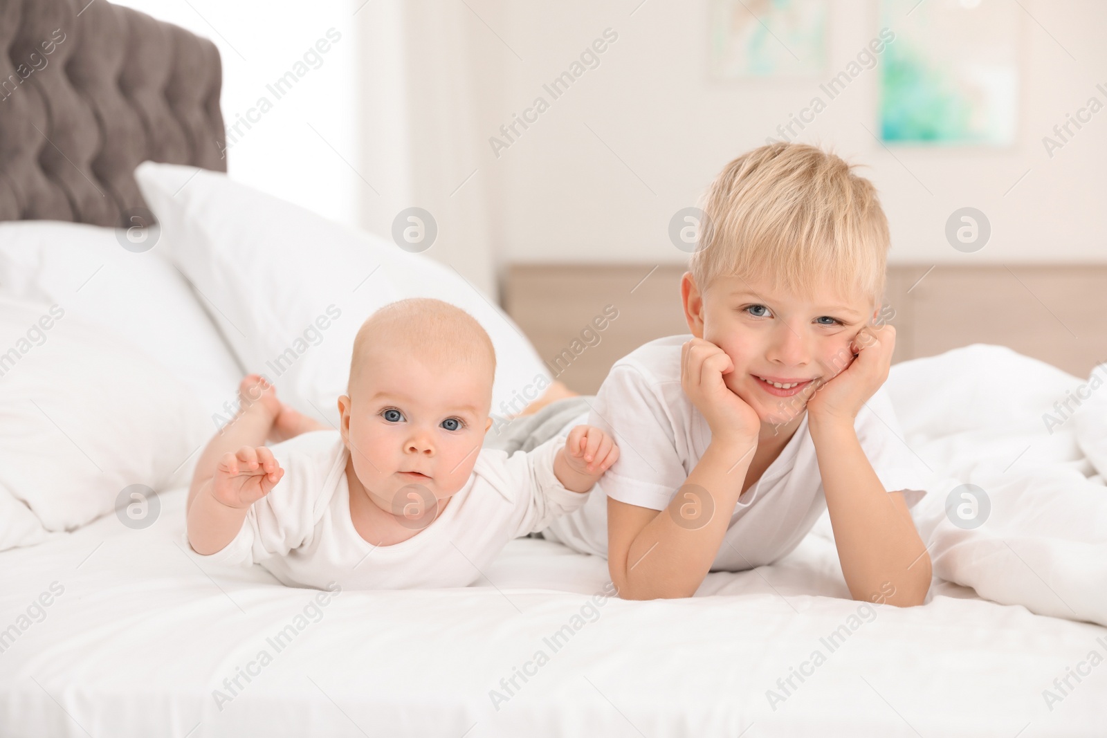 Photo of Cute boy with his little sister lying on bed at home