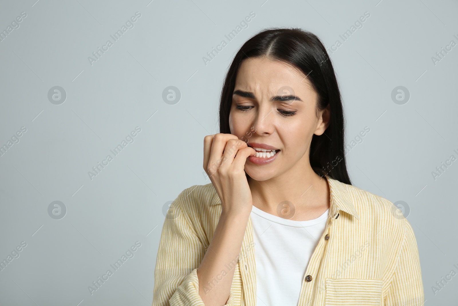 Photo of Young woman biting her nails on light grey background. Space for text