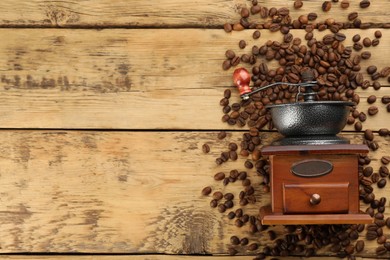 Vintage manual coffee grinder with beans on wooden table, flat lay. Space for text