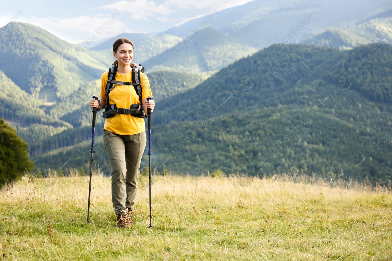 Photo of Woman with backpack and trekking poles hiking in mountains. Space for text