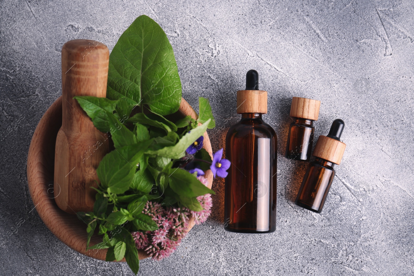 Photo of Glass bottles of essential oil and mortar with different wildflowers on light grey table, flat lay