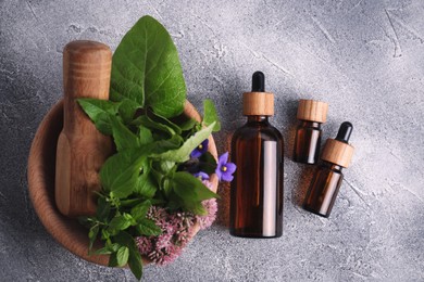 Glass bottles of essential oil and mortar with different wildflowers on light grey table, flat lay