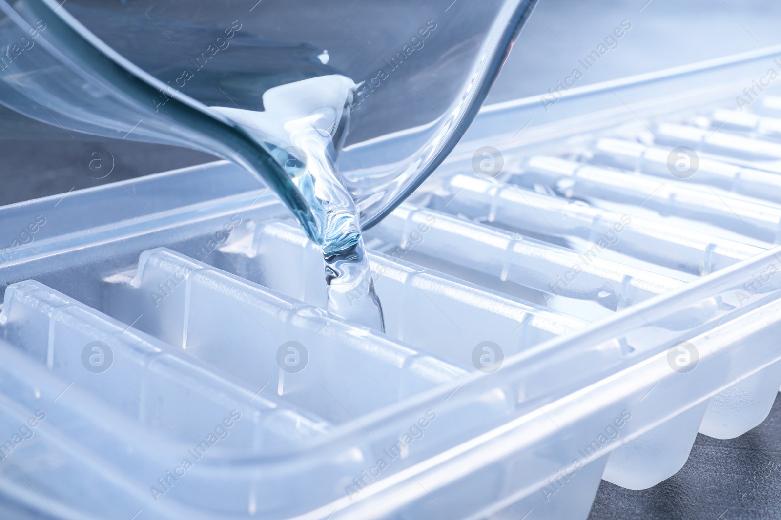 Photo of Pouring water into ice cube tray on table, closeup