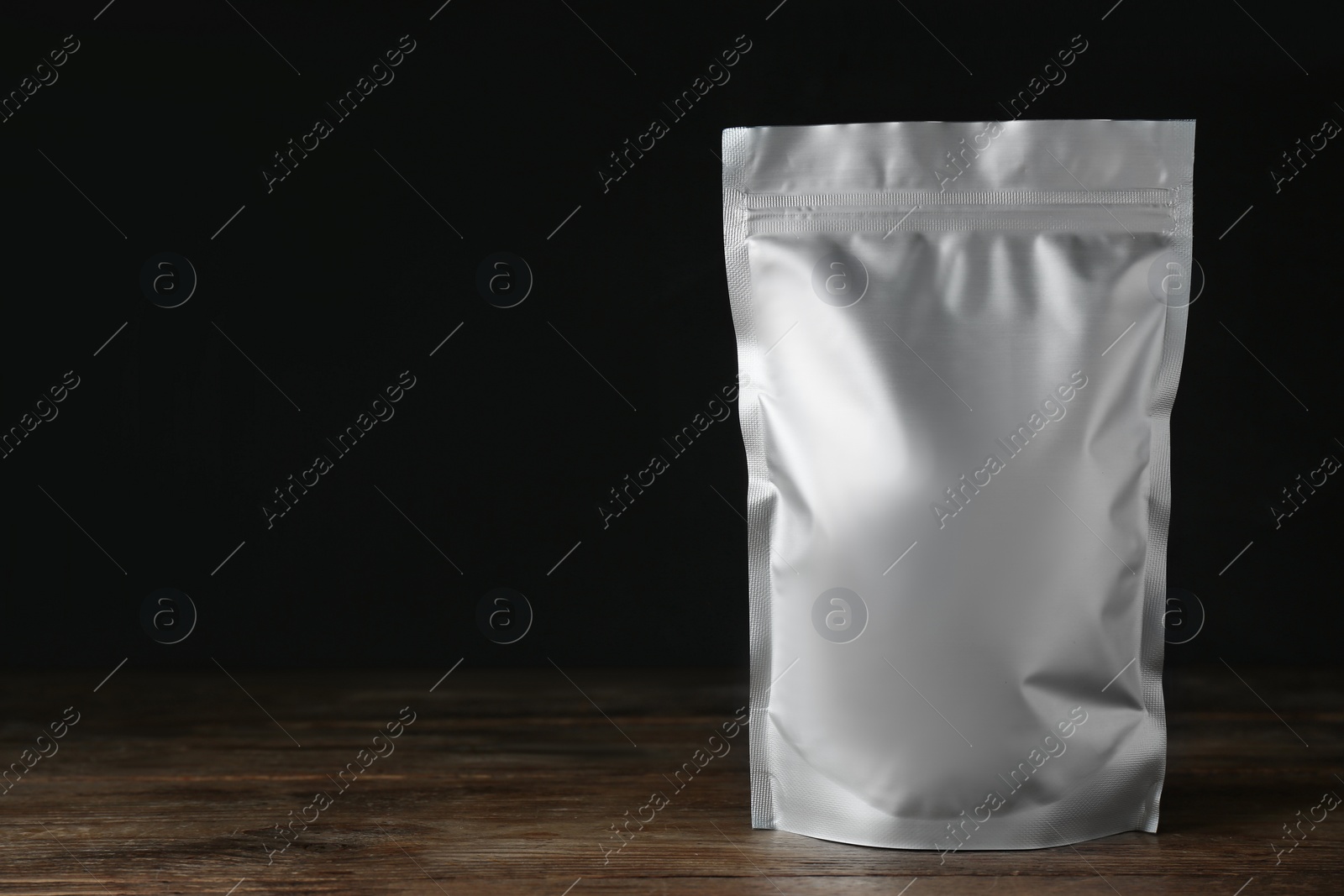 Photo of One blank foil package on wooden table against dark background. Space for text