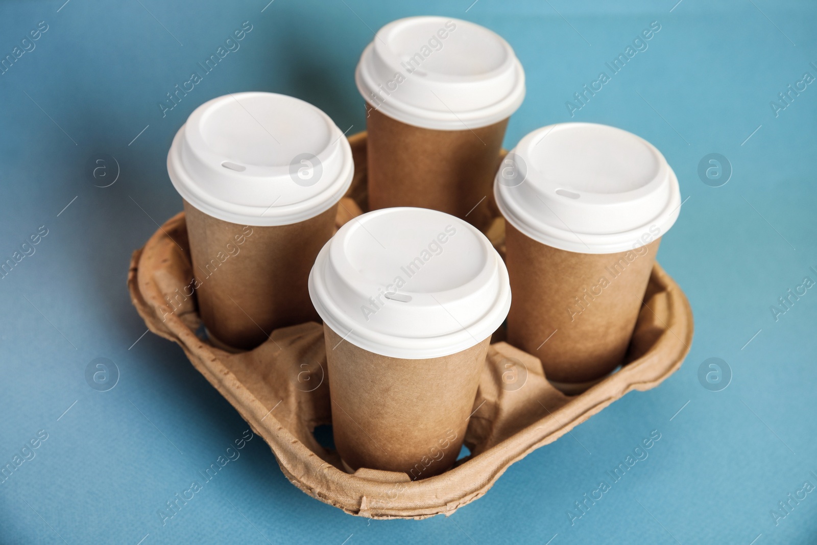 Photo of Takeaway paper coffee cups with plastic lids in cardboard holder on blue background