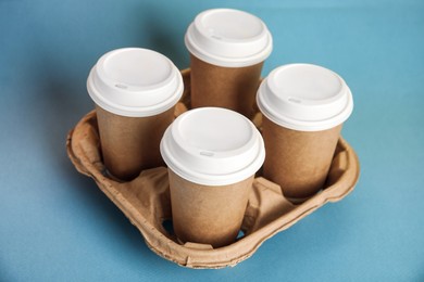 Photo of Takeaway paper coffee cups with plastic lids in cardboard holder on blue background
