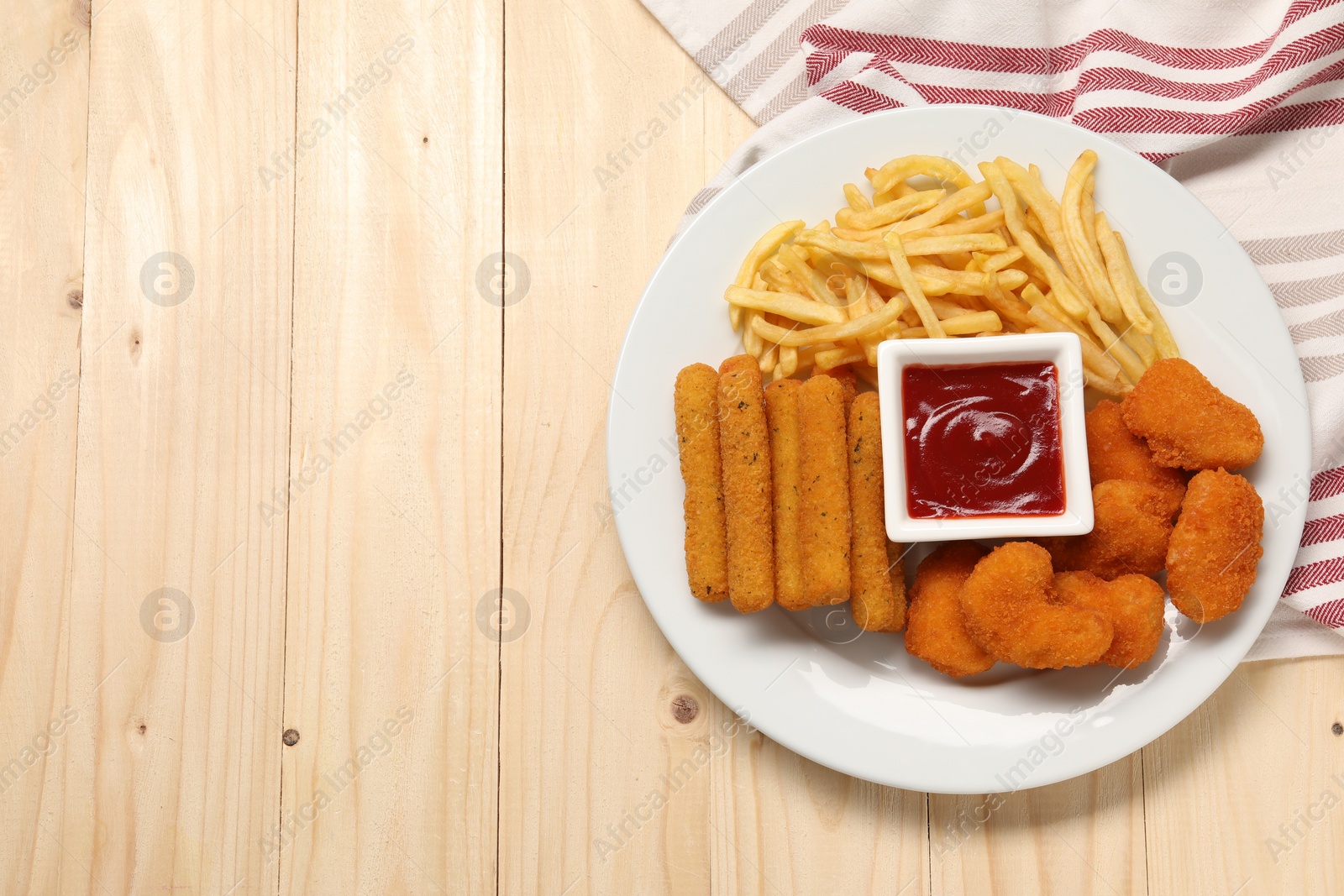 Photo of Plate with tasty ketchup, fries, chicken nuggets and cheese sticks on wooden table, top view. Space for text