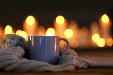Cup of hot drink and knitted cloth against blurred background. Winter atmosphere