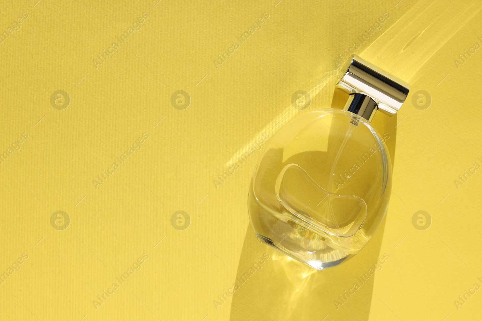 Photo of Luxury women's perfume. Sunlit glass bottle on yellow background, top view. Space for text