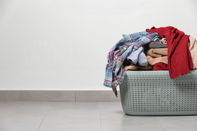 Photo of Laundry basket with clothes near white wall. Space for text