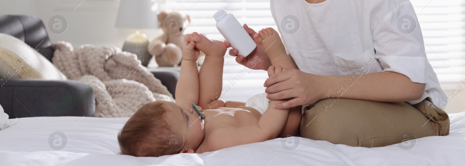 Image of Mother with bottle of dusting powder and her cute baby at home. Banner design