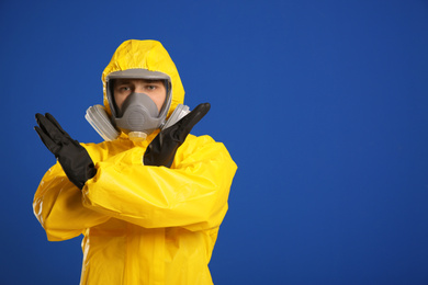 Photo of Man in chemical protective suit making stop gesture on blue background, space for text. Virus research