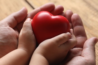 Father and his child holding red decorative heart at wooden table, closeup