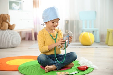 Photo of Cute child imagining himself as doctor while playing with stethoscope and toy bear at home