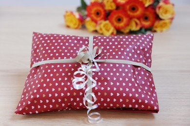 Photo of Parcel wrapped in heart patterned paper and flowers on wooden table, closeup