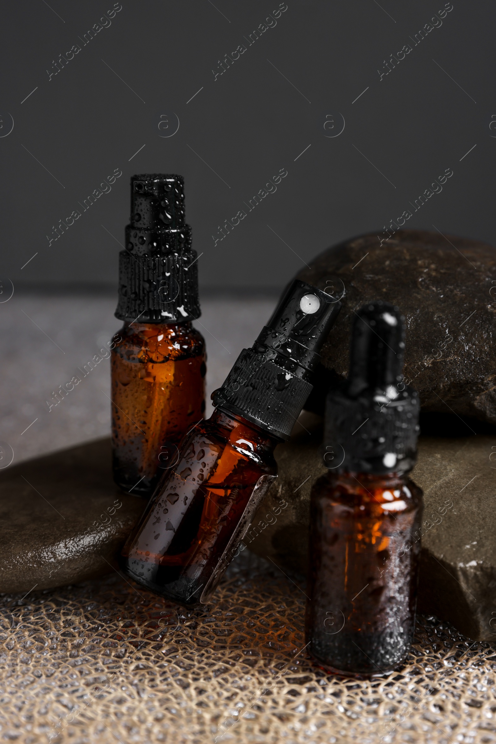 Photo of Bottles of organic cosmetic products and stones on wet surface