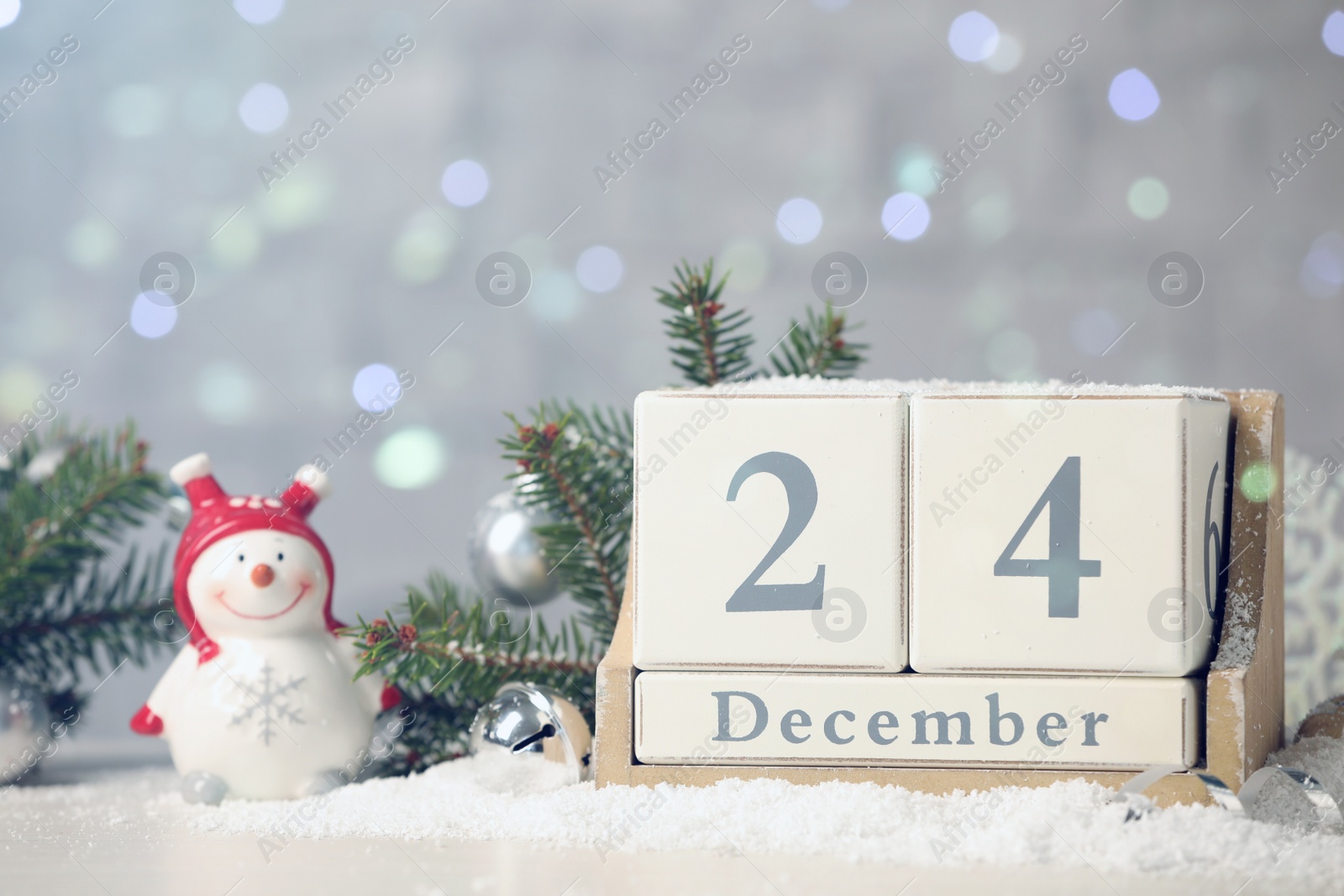 Photo of December 24 - Christmas Eve. Wooden block calendar and festive decor on snow against blurred lights