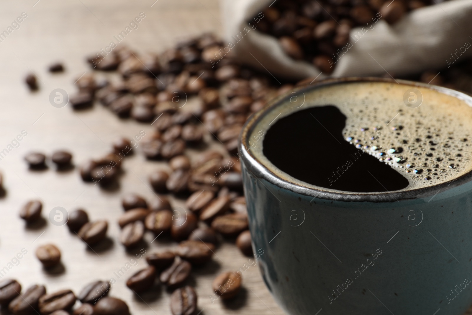 Photo of Cup of aromatic hot coffee and beans on wooden table, closeup. Space for text