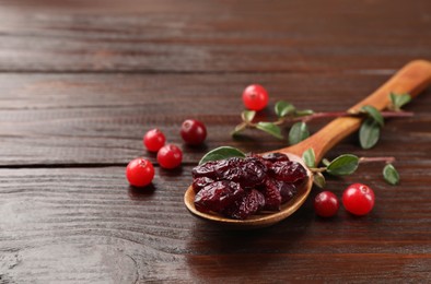 Photo of Tasty dried cranberries in spoon, fresh ones and leaves on wooden table. Space for text