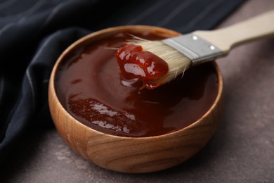 Photo of Marinade in bowl and basting brush on brown table, closeup