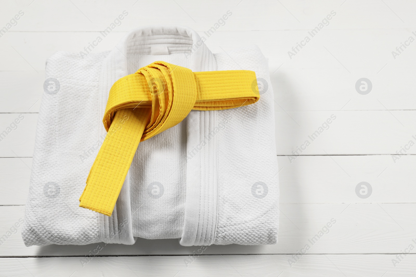 Photo of Yellow karate belt and white kimono on wooden background, space for text
