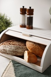 Wooden bread basket with freshly baked loaves on white marble table in kitchen