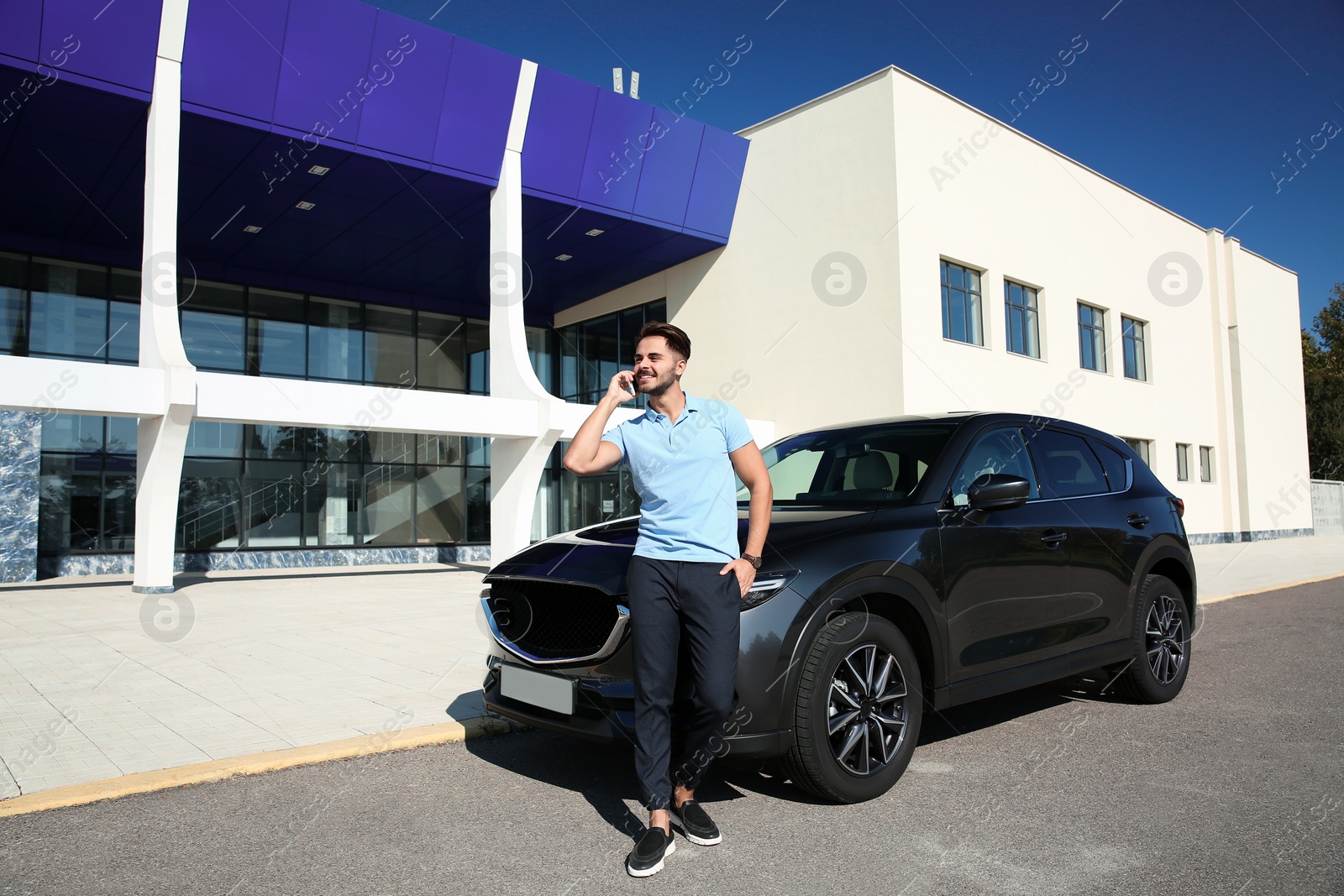 Photo of Young man talking on phone near modern car, outdoors