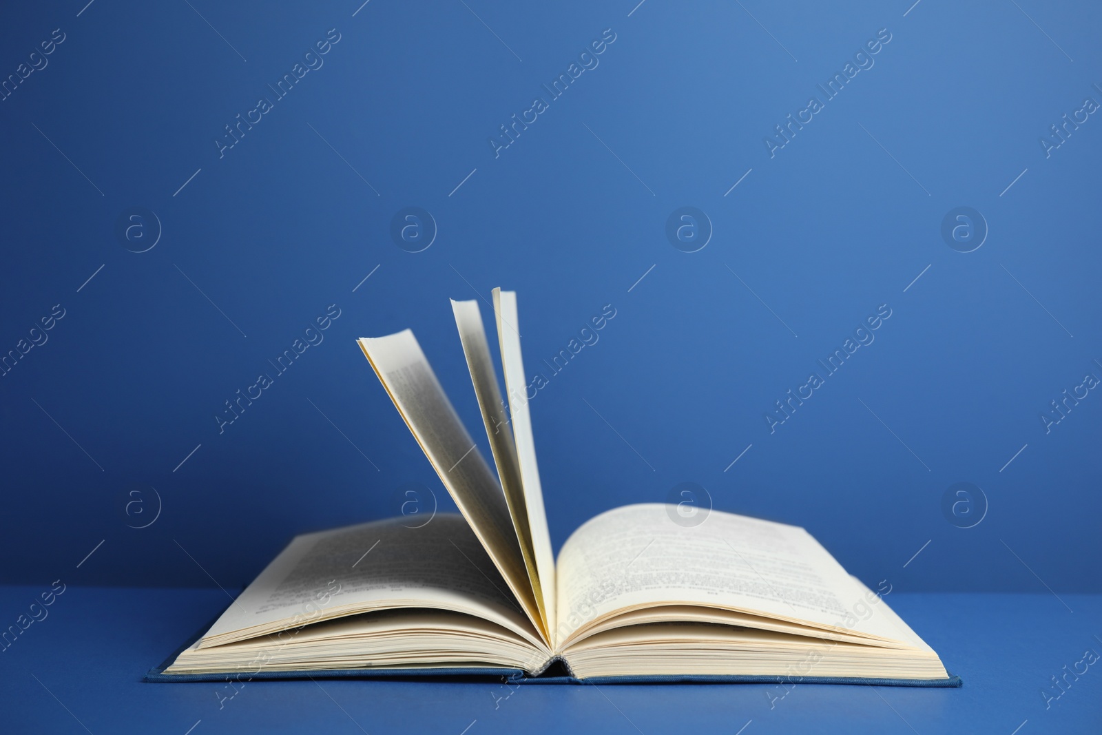 Photo of Open old hardcover book on blue background. Space for text