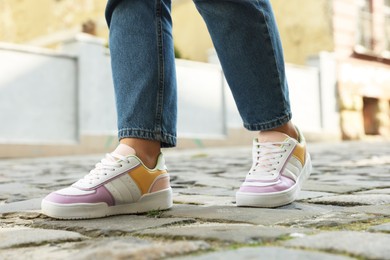 Woman in stylish sneakers walking on city street, closeup