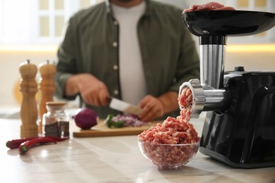 Photo of Closeup view of man cutting onion in kitchen, focus on meat grinder
