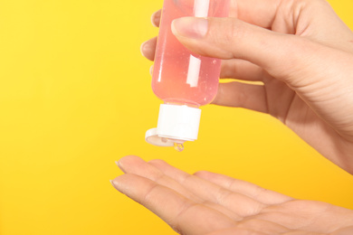 Woman applying antiseptic gel on yellow background, closeup