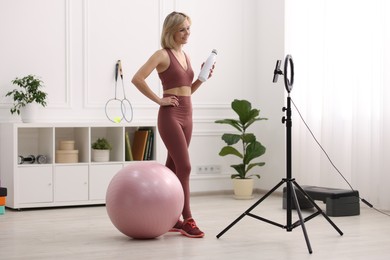 Smiling sports blogger holding bottle while streaming online fitness lesson at home