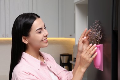 Happy woman with dried flowers and silicone vase attached to refrigerator in kitchen