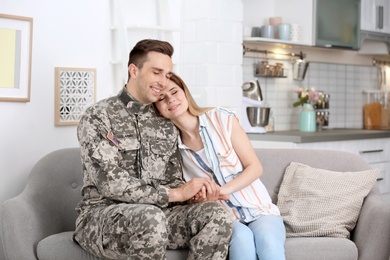 Photo of Young man in military uniform with his wife on sofa at home