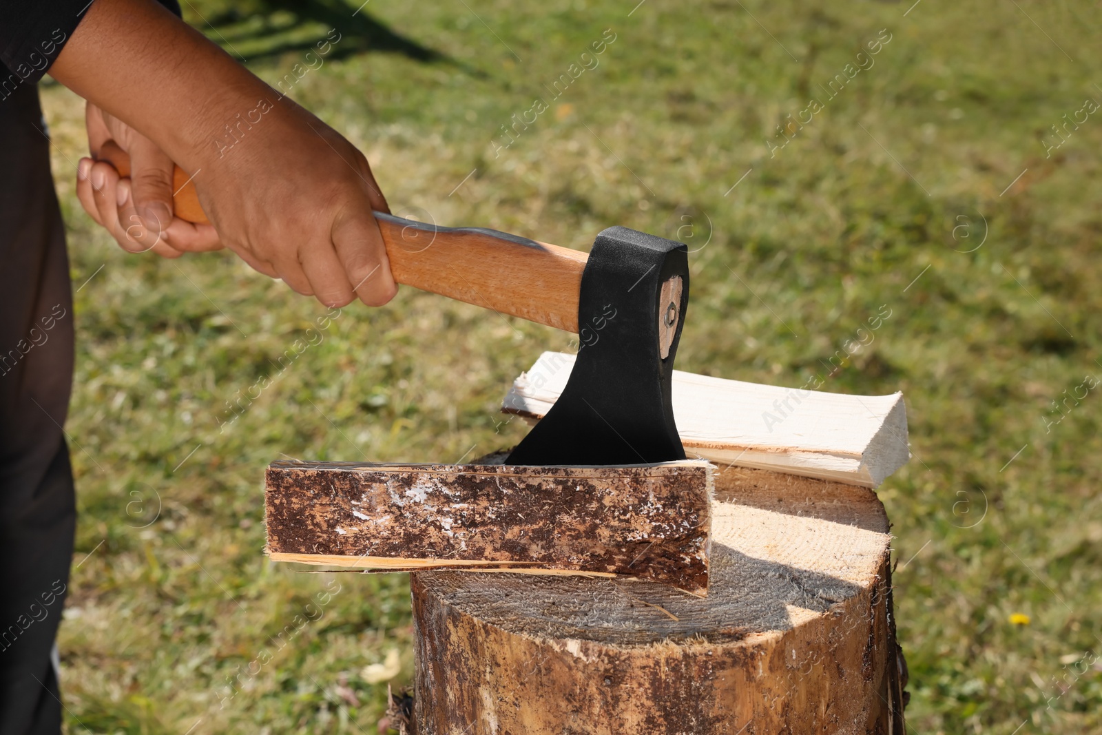Photo of Man cutting firewood with axe outdoors, closeup