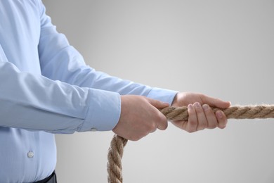 Photo of Dispute concept. Man pulling rope on light grey background, closeup