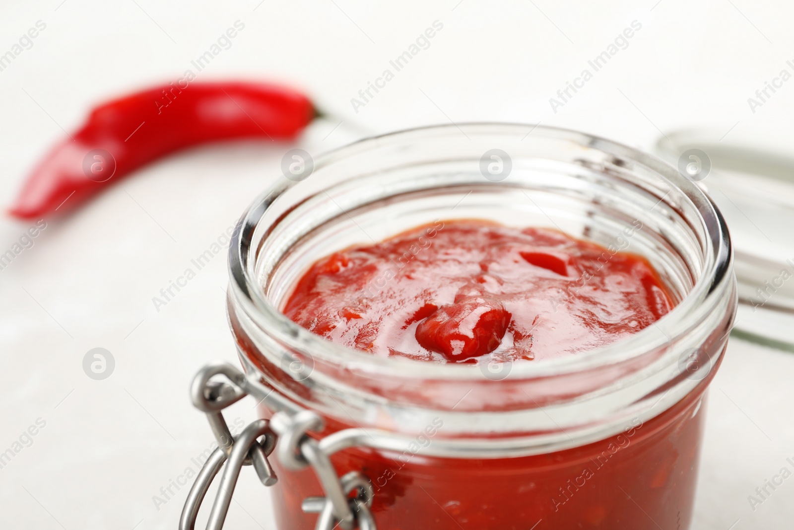 Photo of Jar with spicy chili sauce on light table, closeup