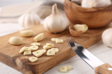 Photo of Aromatic cut garlic, cloves, bulbs and knife on white wooden table, closeup