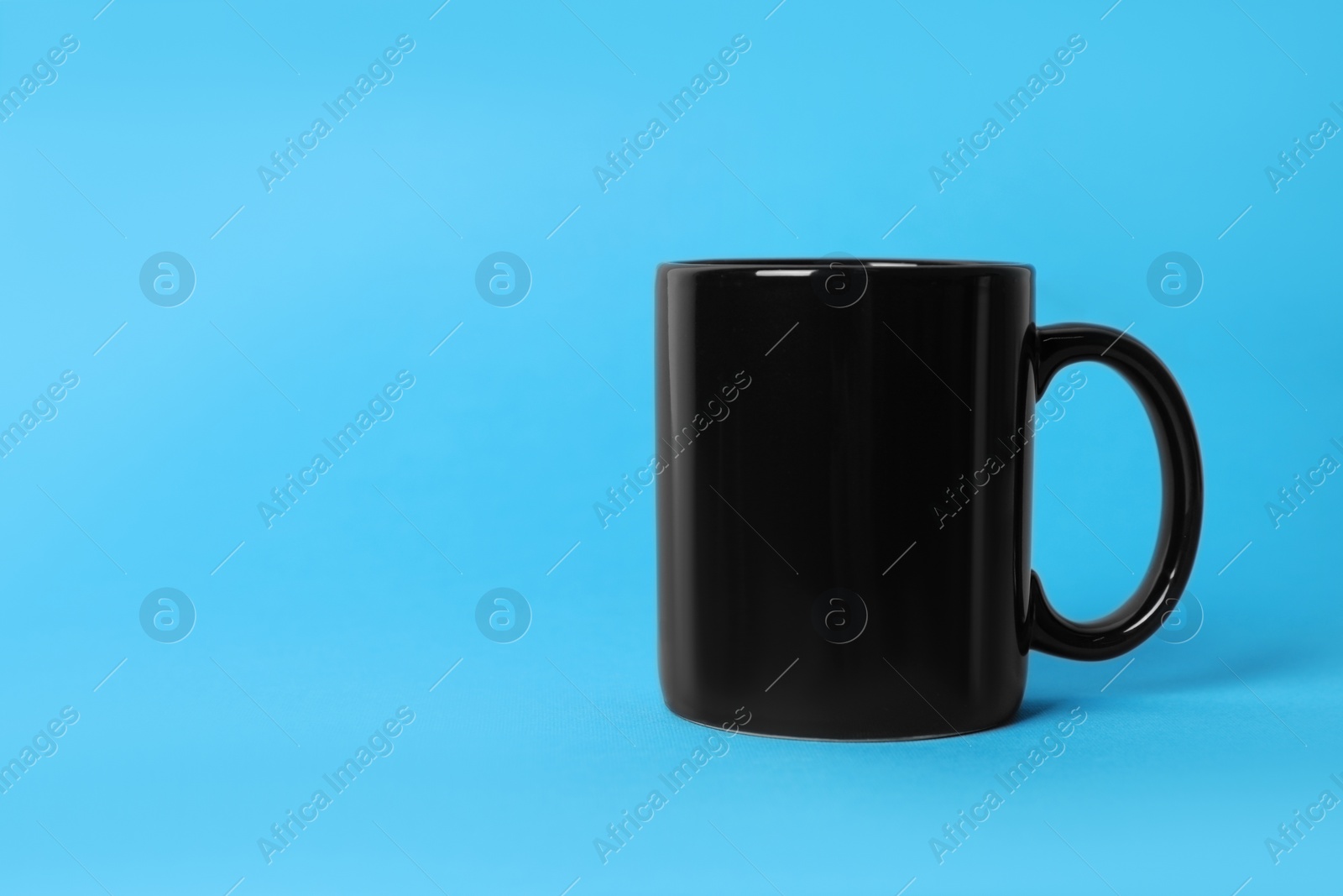 One black ceramic mug on light blue background. Space for text Photo of One black ceramic mug on light blue background. Space for text