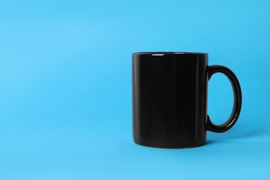 Photo of One black ceramic mug on light blue background. Space for text