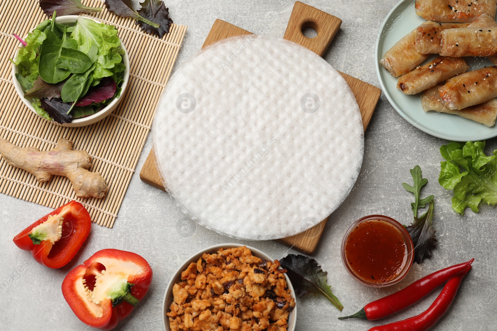 Photo of Rice paper, ingredients and tasty fried spring rolls on grey table, flat lay